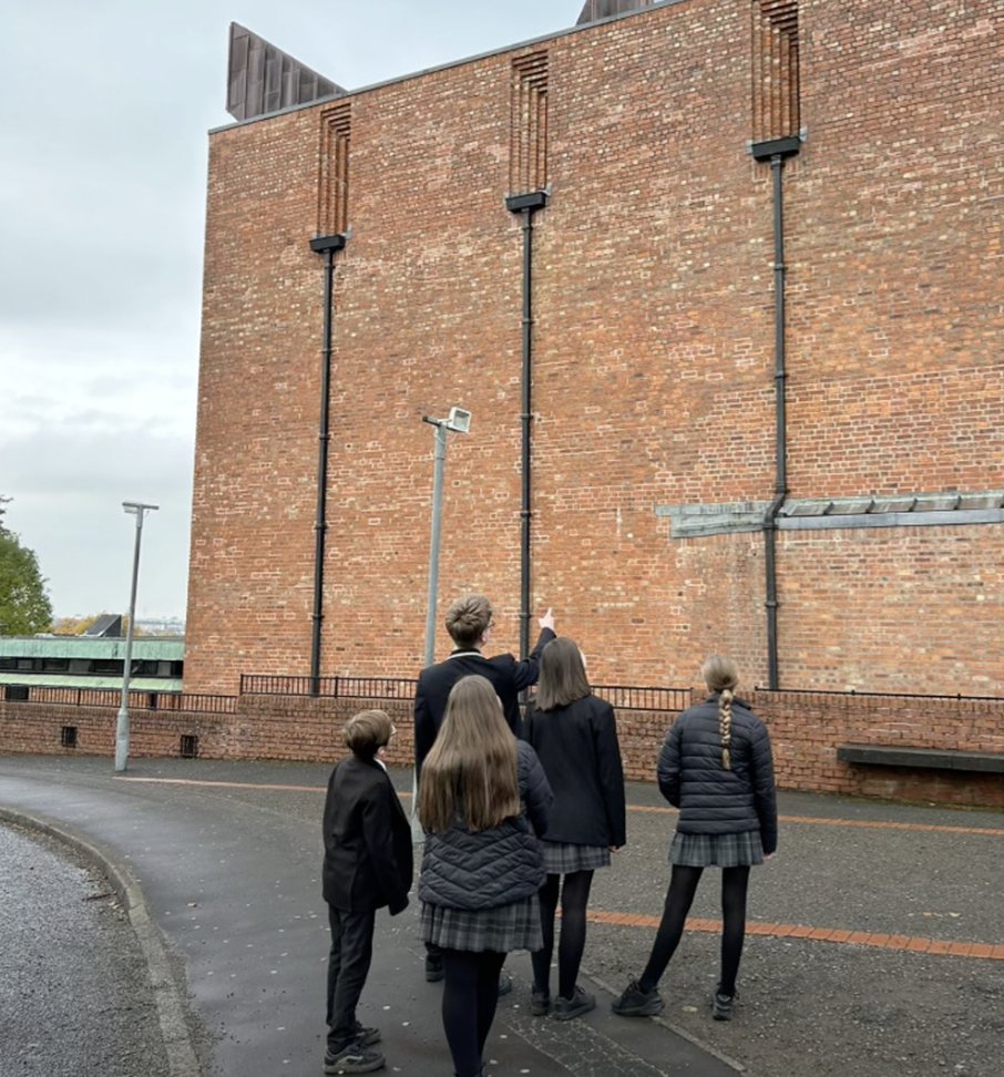 Pupils in school uniform looking up at a tall brick building.