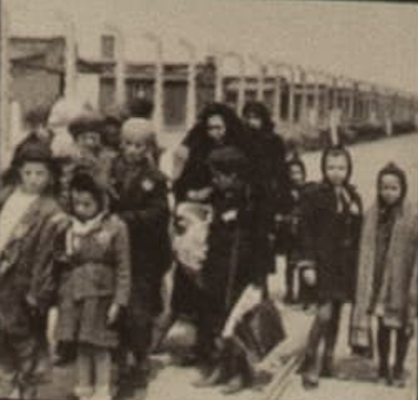 Black and white photograph of women and children in winter coats walking along a railway line, some wearing a star on their clothes.